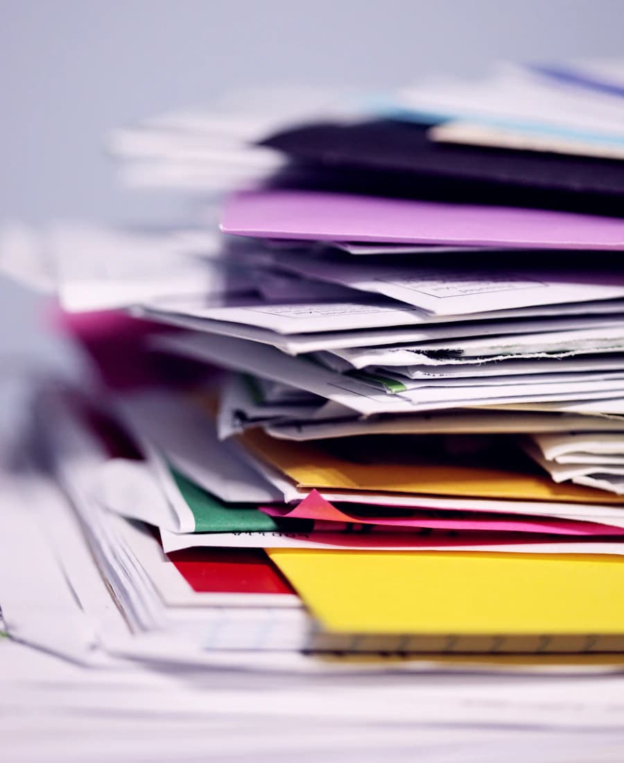 A tall, untidy stack of paper forms and folders in mixed colours.